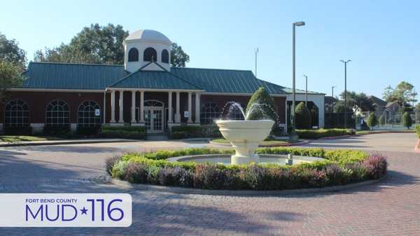 Modern community building with a central dome, fountain, and flower beds, featuring a sign for Fort Bend County MUD 116 in the foreground under a clear sky.